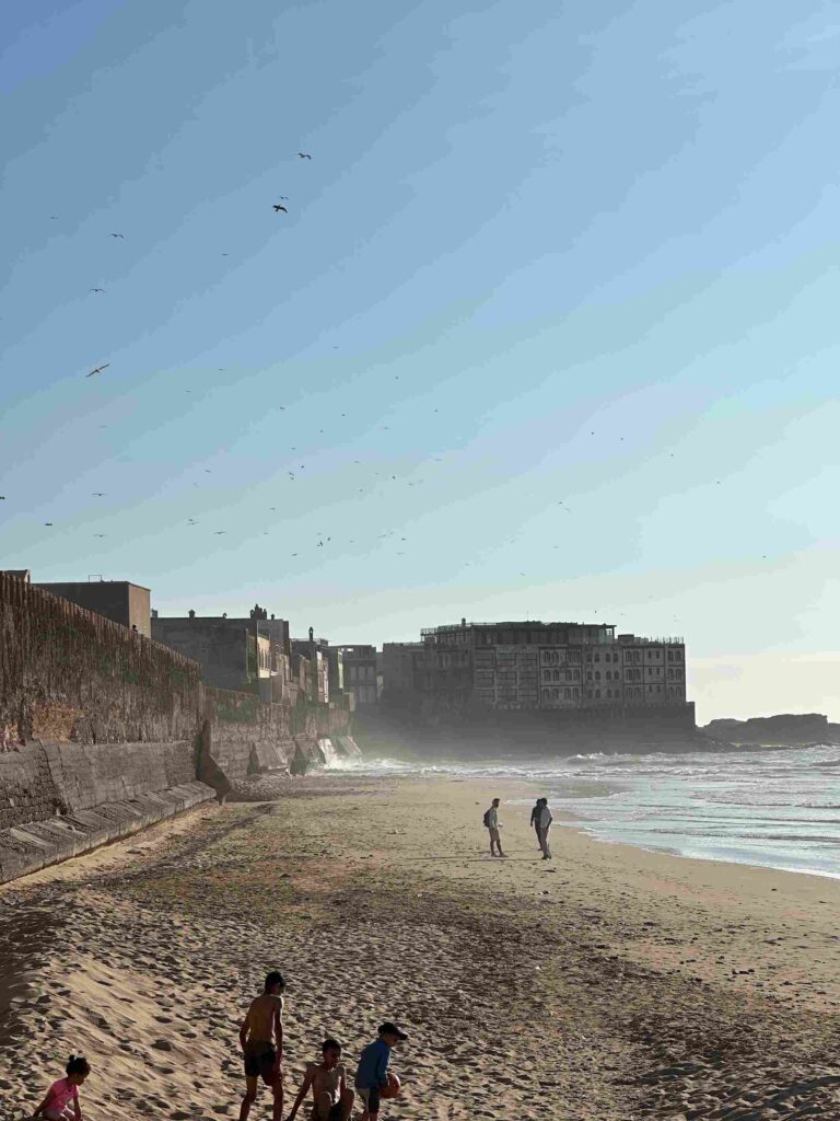 Vue des remparts d’Essaouira avec l’océan Atlantique en arrière-plan et des personnes profitant de la plage